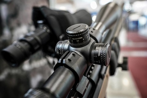 Black shooting scope optics mounted on rifle displayed at weapons exhibition fair, closeup detail