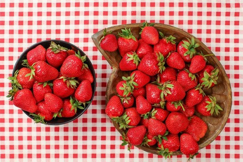 Top down view, strawberries in black and wooden carved bowl on red gingham pattern tablecloth,