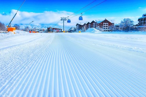 Close-up groomed snow at Bansko resort, Bulgaria panorama with ski slope and cable car lift