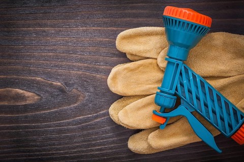 Spray nozzle and leather working safety gloves on wooden board gardening concept