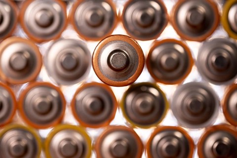 Multiple used AA alkaline batteries are seen arranged in a pile. Closeup front view from the plus