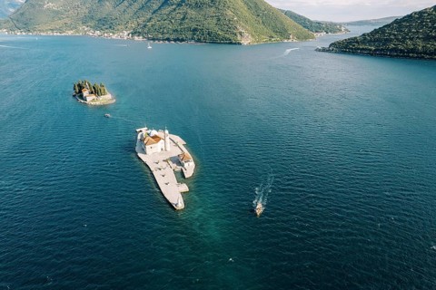 Motor boat sails on the sea past the island of Gospa od Skrpjela. Montenegro. Drone.