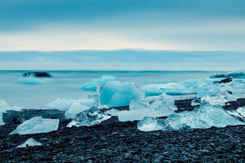 Ice formations along the ocean shoreline under a serene blue sky, creating a cold feeling,