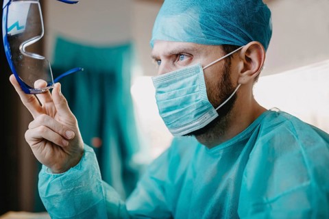A surgeon attentively holds his protective glasses, wearing a mask