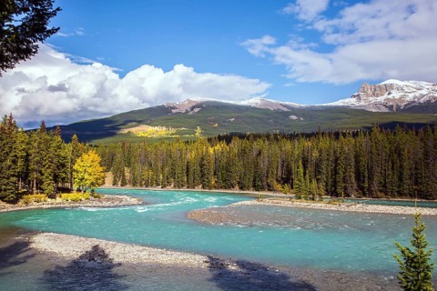 Mountain river with icy melt water from glaciers. Mountain peaks are covered with snow. The Rocky
