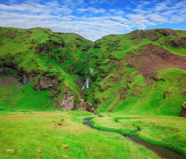 Basalt mountains covered in green moss and grass . Gorgeous cascading waterfall from melting
