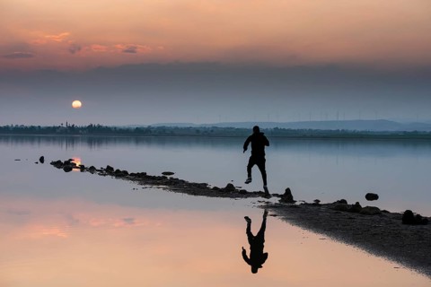 Unrecognised person running to reach the sun. Idyllic winter sunset at a lake. Silhouette