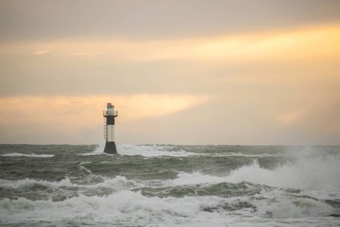 A lighthouse stands in the storm. Wild sea in the evening. Sunset on a coast with many rocks in the