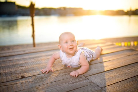 A child a boy, one year old, blond man lies on his stomach on wooden dock, pier in striped clothes,