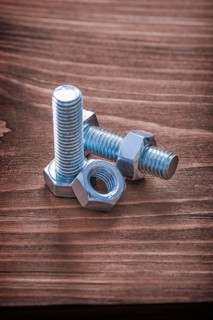 Stainless bolts and nuts on brown wooden board construction concept