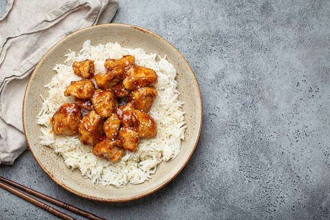 Chinese sweet and sour sticky chicken with sesame seeds and rice on ceramic plate with chopsticks