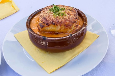 Portion of lasagna bolognese in a terracotta ramekin lay on a white plate