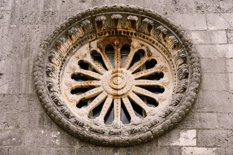 Rose window with ornaments and patterns on the dark stone wall of the church.
