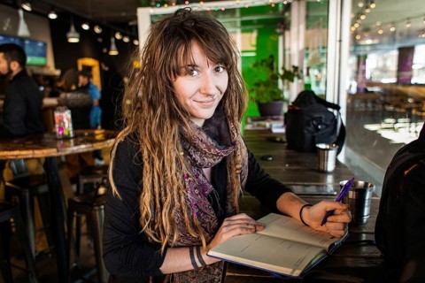 Portrait of smiling beautiful girl with dreadlocks and tattoos. Writing on a notebook with a pen in
