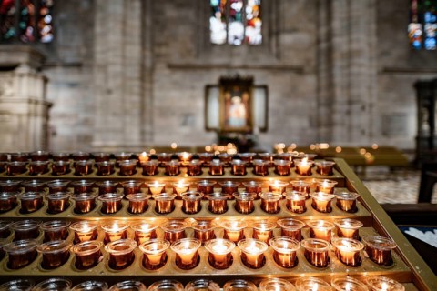 Votive candles are burning on a stand in the Duomo Cathedral. Close-up.