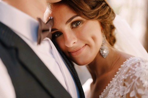 Close-up portrait of a bride looking at the camera, laid her head on the groom's chest. Beautiful