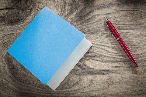 Vintage blue notepad red ballpoint pen on wooden board