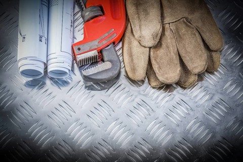 Pipe wrench construction plans leather safety gloves on corrugated metal background building