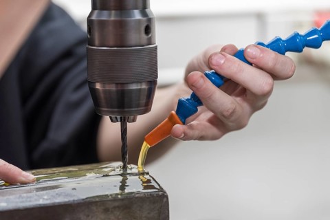 Skilled worker drills hole in steel with metal drill using cooling lubricant