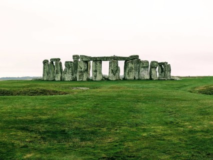 Warm-toned image of Stonehenge on a grassy field under a cloudy sky. Salisbury, England, United