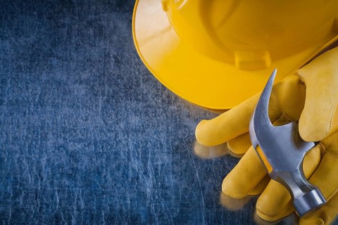 Pair of protective gloves hard hat and claw hammer on scratched metallic background construction
