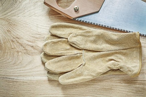 Leather protective gloves handsaw on wooden board construction concept