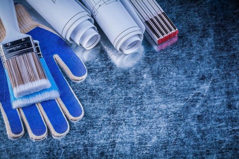 Wooden meter paint brush safety gloves blueprints on metallic background
