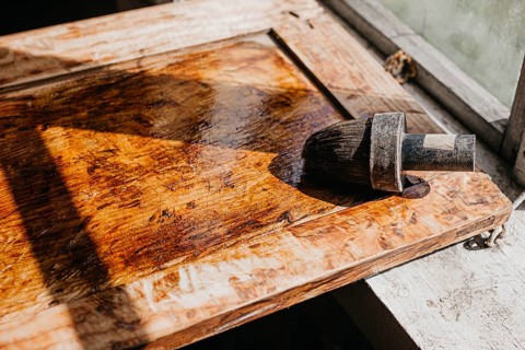 Varnished wooden surface under sunlight, highlighting texture with brush nearby