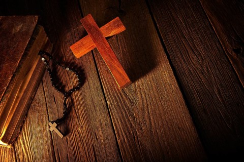 Christian cross on wood bible and rosary beads over wooden vintage background