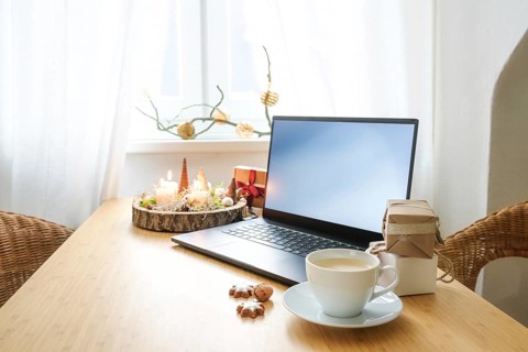 Laptop on a wooden desk by the window in an attic apartment. Gifts, advent candles, Christmas