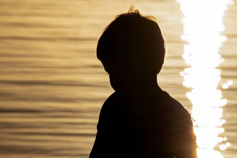 Silhouette of little boy by the sea at sunset