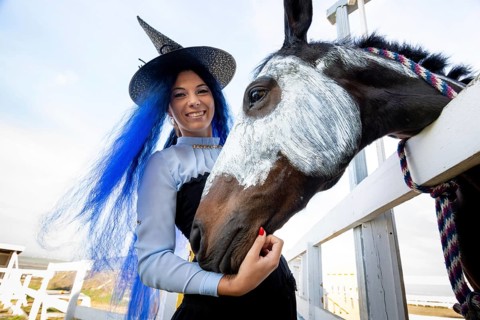 A girl dressed as a witch stands next to a horse on which a skeleton is drawn for the celebration