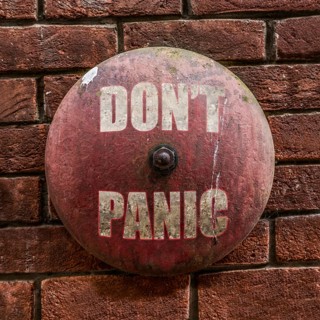 Isolated Rustic Vintage Red Alarm Bell With The Words Don't Panic In White Against A Red Brick Wall