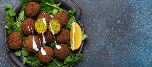 Plate of fried falafel balls served with fresh green cilantro and lemon top view on rustic concrete
