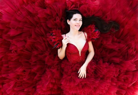 From above of lying beautiful young brunette female in luxurious red evening gown looking at camera
