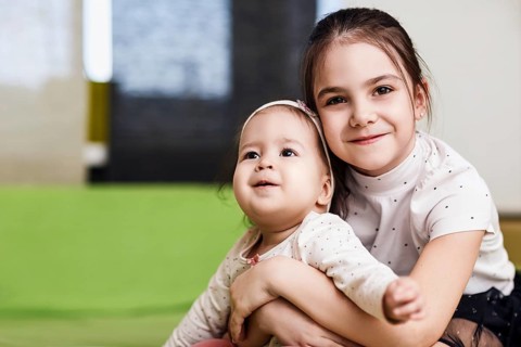 Elder sister with her little baby sister hugging in the bedroom. Siblings love