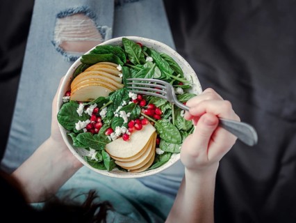 Woman in jeans holding vegan salad bowl with spinach, pear, pomegranate, cheese. Vegan breakfast,