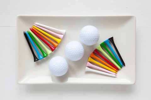 White ceramic dishes with golf balls and wooden tees on over white background, rectangle dish