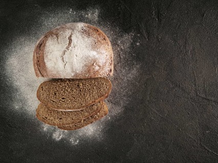Sliced homemade sourdough rye bread with rye flour on black textured background. Top view or