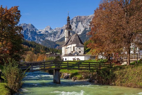Parish church of St. Sebastian in autumn with the river Ramsauer Ache, behind mountains of the