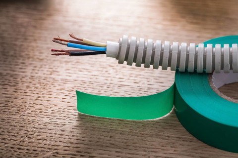 Electric cable in corrugated pipe on roll of green insulating tape