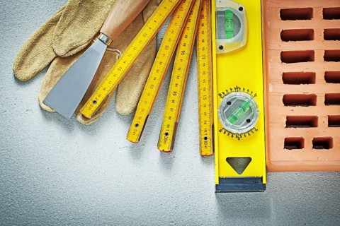 Red brick protective gloves putty knife construction level wooden meter on concrete background