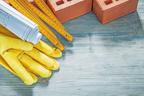 Composition of red bricks protective gloves blueprints wooden meter on wood board construction