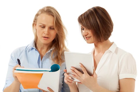 Two colleagues looking at notebook. White background. Isolated, studio shot