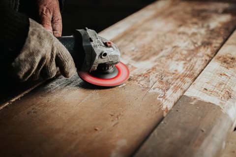Gloved hands using a sanding tool on wood, focusing on surface texture and craftsmanship