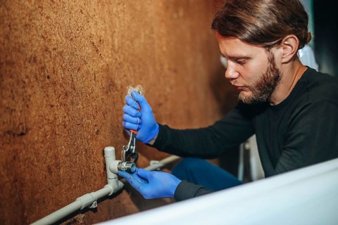 Person using a wrench on a pipe connection while wearing gloves