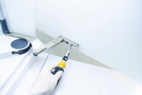 Close-up of a gloved hand fixing a cabinet hinge with a screwdriver