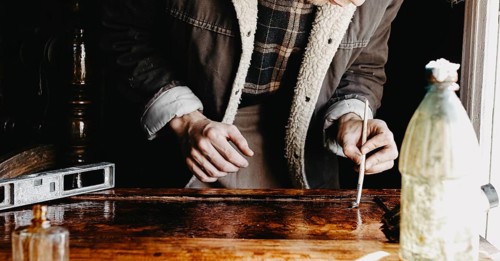 A person concentrated on applying varnish on wood with a bottle nearby