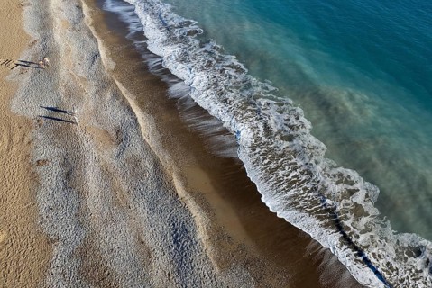 Aerial drone point of view of person walking on sand in a beach. Stormy waves idyllic beach in