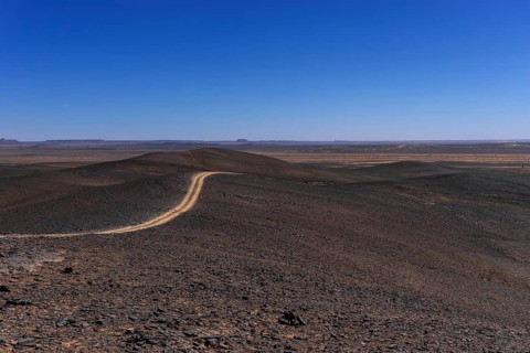 A view of a dirt road leading through the rock and sand desert of southeastern Morocco mear